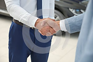 Young salesman shaking hands with client in modern car dealership