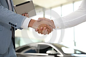 Young salesman shaking hands with client in modern car dealership