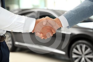 Young salesman shaking hands with  in modern car dealership, closeup