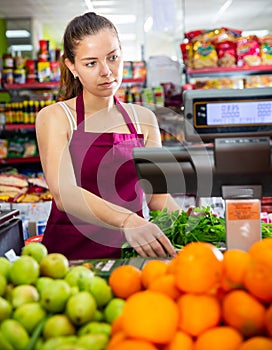 Young saleswoman weighs greens on a scale