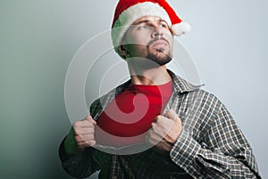 Young Santa Claus rips his shirt on his chest like a superhero. the man in the Santa hat