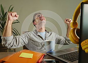 Young satisfied and confident business man excited gesturing on victory as a winner working at home office with laptop computer on