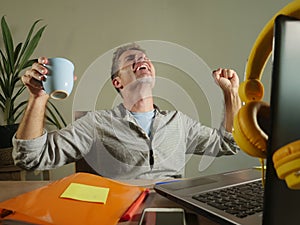 Young satisfied and confident business man excited gesturing on victory as a winner working at home office with laptop computer on