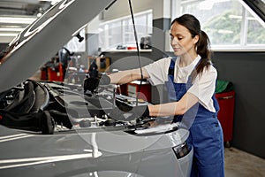 Young satisfied female mechanic fixing engine at service car garage