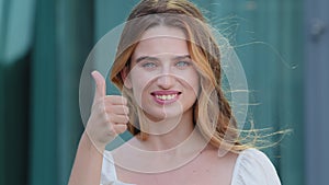 Young satisfied Germanic Scandinavian woman smiling with white teeth showing thumbs up looking at camera. Happy white