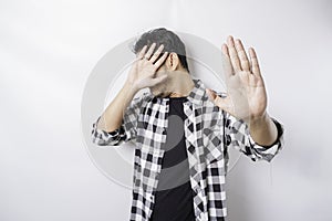 Young scared Asian man isolated on white background, looks depressed, face covered by fingers frightened and nervous