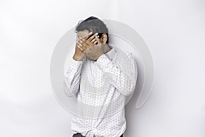 Young scared Asian man isolated on white background, looks depressed, face covered by fingers frightened and nervous