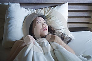 Young scared and stressed Asian Chinese woman lying in bed suffering nightmare in fear and panic grasping blanket covering her hor