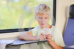 Young school boy in train with mobile phone