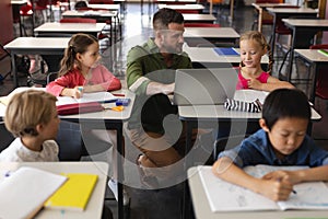 Young school teacher helping girl with study on laptop in classroom