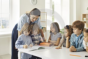 School teacher helping her happy little students who are writing in their notebooks