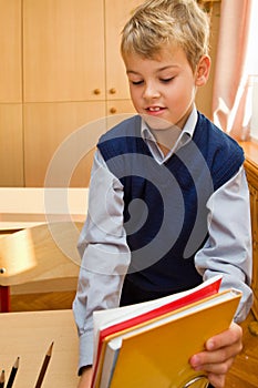 Young schoolboy packs books Behind a school desk