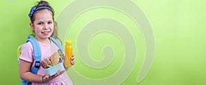 Young schoolgirl with lunch box and a bottle of juice on a green background.