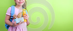 Young schoolgirl with lunch box and a bottle of juice on a green background. Little girl with a school backpack and a