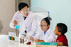 Young scientist holding a flask and teaching two African American mixed kids in chemistry lab
