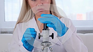 Young scientist laboratory assistant looks through a microscope in the laboratory. A young scientist is doing some