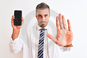 Young scientist man showing smartphone screen over isolated background with open hand doing stop sign with serious and confident