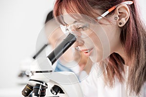 Young scientist in protective goggles working with microscope in chemical lab