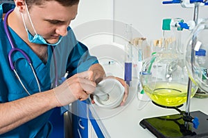 Young scientist in uniform wearing a mask preparing powder on ce