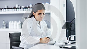Young scientist using a computer and microscope in a lab. Female pathologist analyzing medical samples while doing