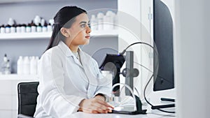 Young scientist using a computer and microscope in a lab. Female pathologist analyzing medical samples while doing