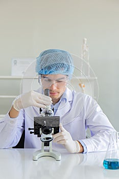 Young Scientist using Microscope in Laboratory. Male Researcher wearing white Coat sitting at Desk and looking at Samples by using