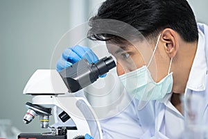 Young scientists wear gloves using a microscope to see coronavirus Covid-19 in a laboratory. Looking cell virus von plate.