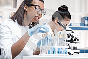 Young scientists working with microscope and test tubes in chemical laboratory