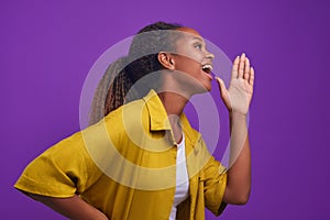 Young screaming African American woman puts hand near mouth stands in studio