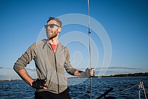 Young seaman on a sailboat standing on a sail boom. Captain of the yacht in the open sea.