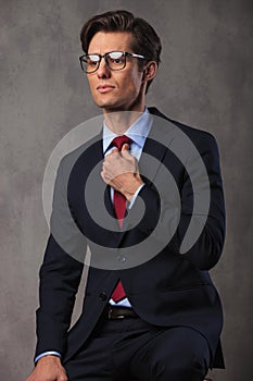 Young seated business man fixing his tie