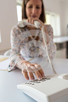 Young secretary sitting at her office desk dialing a telephone number