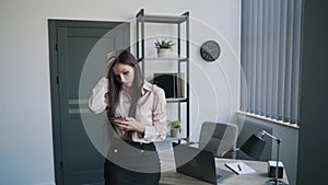 Young secretary worker businesswoman in shirt and skirt searching something on mobile phone in office. Shows different emotions