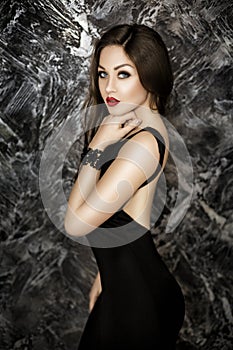 Young and seductive brunette woman with red lipstick in black dress on dark background