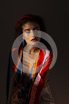 Young seductive woman in colorful top. Portrait with shadows. Beautiful female model standing, posing at camera.