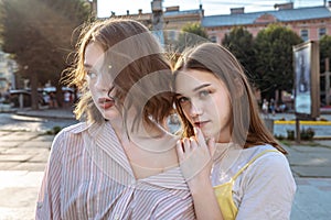 Young sensual brunette girls in casual clothes standing together among the street, girl in white t-shirt holds her hand