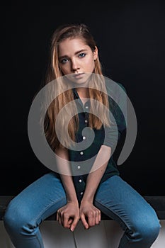 Young sensual girl in checkered green shirt posing on black background while sitting and holding hands in front of her