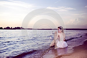 Young Sensual Sea Mermaid Blond Woman With Artistic Makeup and Strasses on Face Posing on Ocean Waves with Silver Crown And Net on