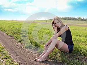 Young sensual smiling blond woman sitting on the grass outdoors