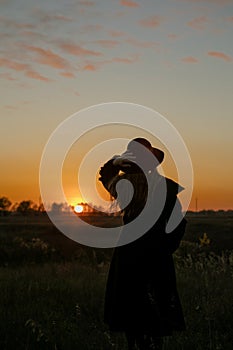 Young sensual woman in black coat standing in the golden autumn field in the evening on sunset