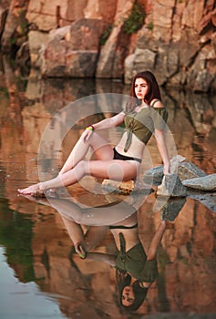 Young sensual woman sitting pensively on stones of lake on the background of rocky mountains