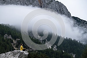 Young serene woman sitting in lotus position on a rock in high mountains and meditating