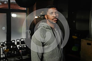 Young serious African American man in grey activewear standing in gym