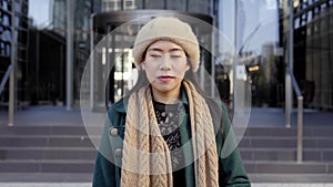 Young serious Asian woman looking camera. Chinese lady outdoors near corporative buildings at the city