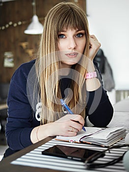 Young serious attractive young woman with pen in hand thinking on plans and writing list to do in notepad enjoying