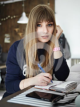 Young serious attractive young woman with pen in hand thinking on plans and writing list to do in notepad enjoying