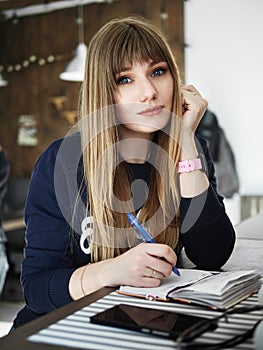 Young serious attractive young woman with pen in hand thinking on plans and writing list to do in notepad enjoying