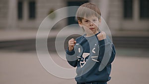 Young serious boy wears casual blue sweatshirt in boxing stance with raised fists looks at you