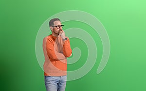 Young serious businessman with hand on chin thinking business ideas on isolated green background