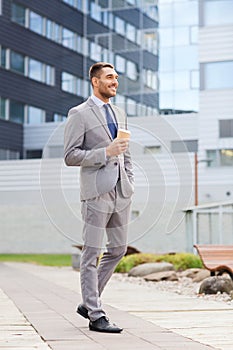 Young serious businessman with paper cup outdoors